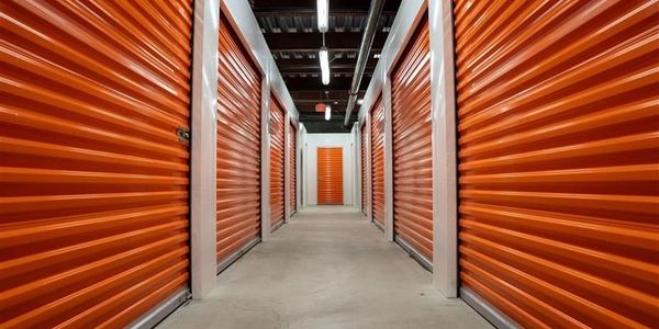 Indoor storage facility hallway with orange roll-up doors on both sides.