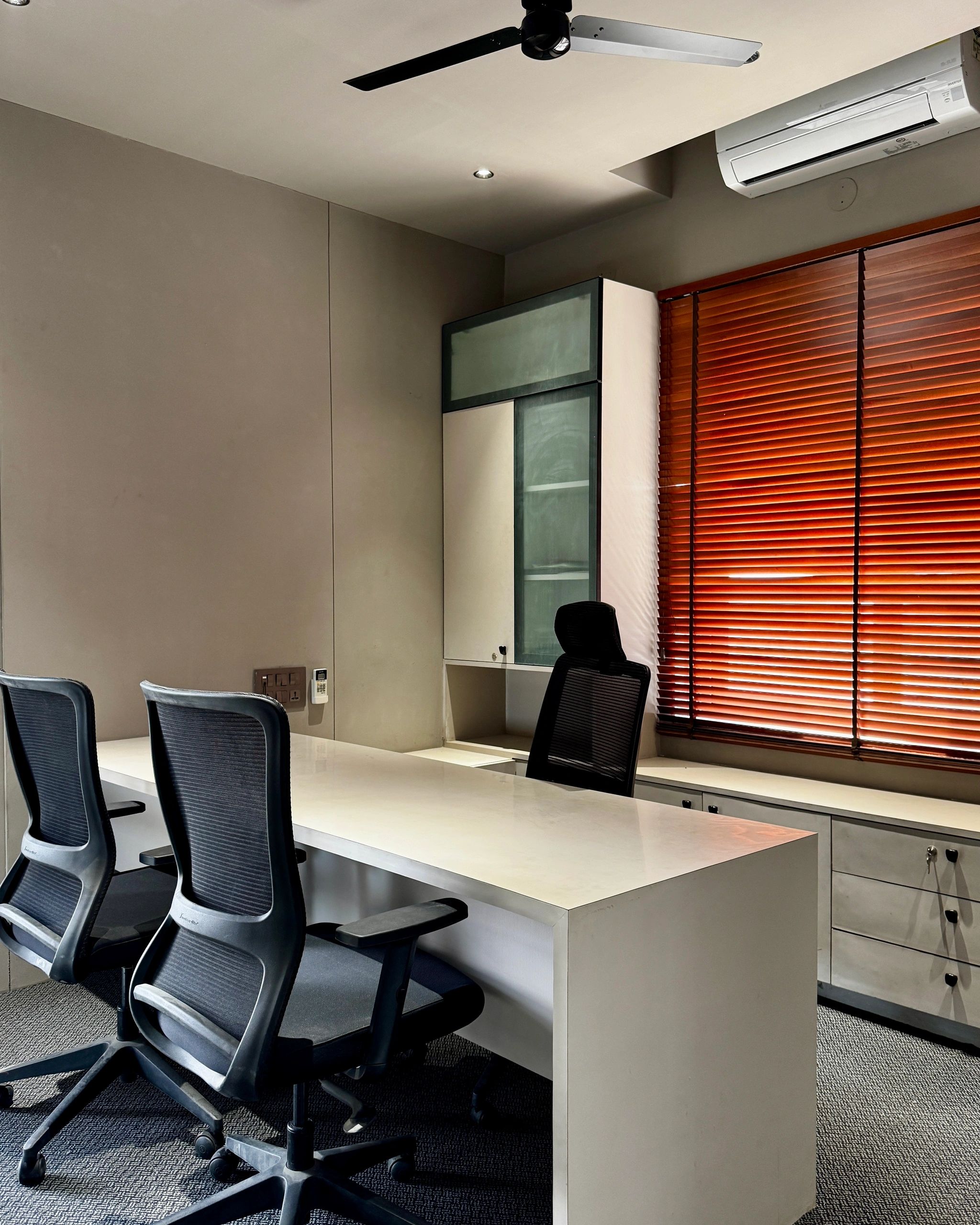 Modern office space with ergonomic chairs, white desk, and warm wooden blinds.