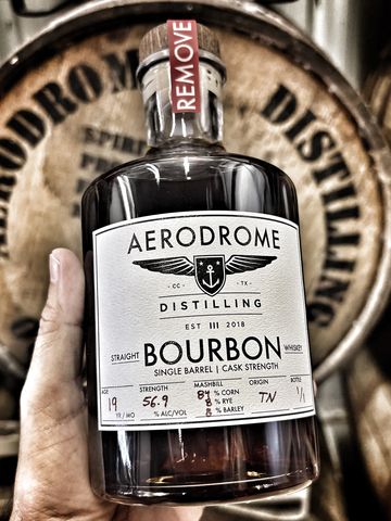 Hand holding a bottle of Aerodrome Distilling Straight Bourbon whiskey.