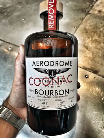 Hand holding a bottle of Aerodrome bourbon whiskey with detailed label.