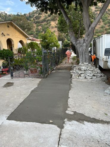 Freshly poured concrete sidewalk leading to a house with hills in the background.