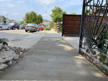 Newly paved sidewalk with parked cars and a decorative iron gate on the right.