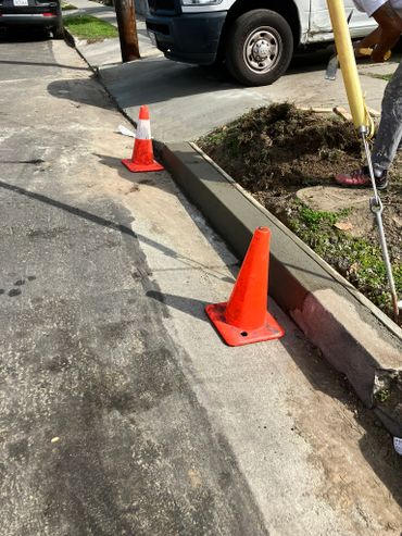 Freshly poured concrete curb with orange safety cones on a street.