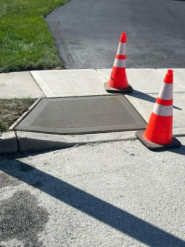 Freshly poured concrete sidewalk patch with two orange safety cones.