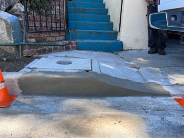 Freshly poured concrete ramp at a driveway with blue stairs in the background.