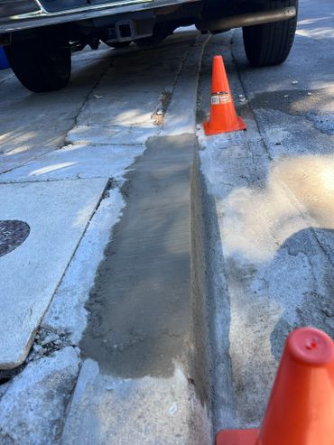 Freshly repaired curb with two orange safety cones and a parked vehicle.