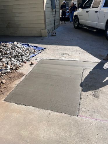 Freshly poured concrete patch on a driveway with people and a truck in the background.