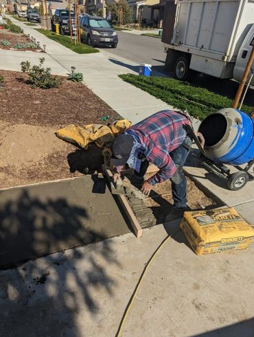Worker smoothing freshly poured concrete on a sidewalk in a residential area.