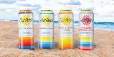 Four colorful Surfside canned beverages on a sandy beach.