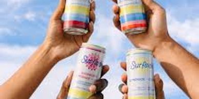 Four hands holding colorful Surfside beverage cans against a blue sky.