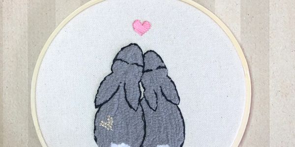 Embroidered bunnies with a heart above them.
