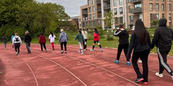 Group of people walking on a red outdoor running track near residential buildings.