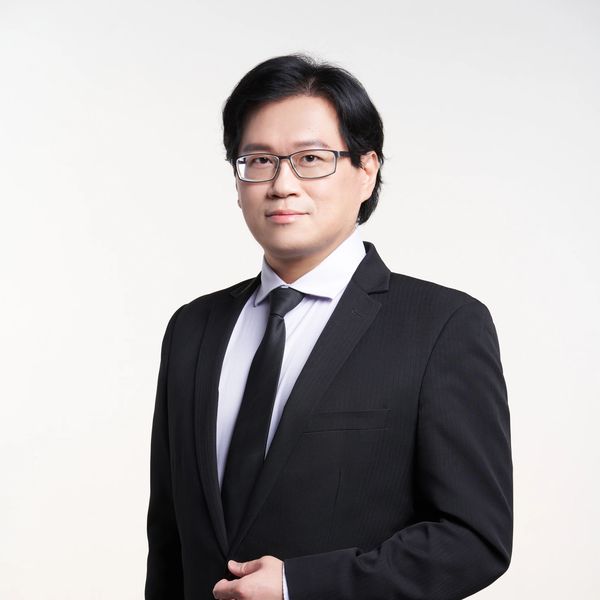 Professional man in a black suit and glasses poses against a white background.
