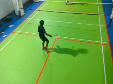 Person playing badminton on an indoor court.