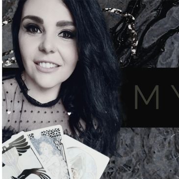 A woman with dark hair smiles, holding tarot cards in front of a dark, textured background.