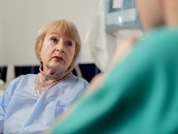 Elderly woman in a medical gown consulting a healthcare professional.