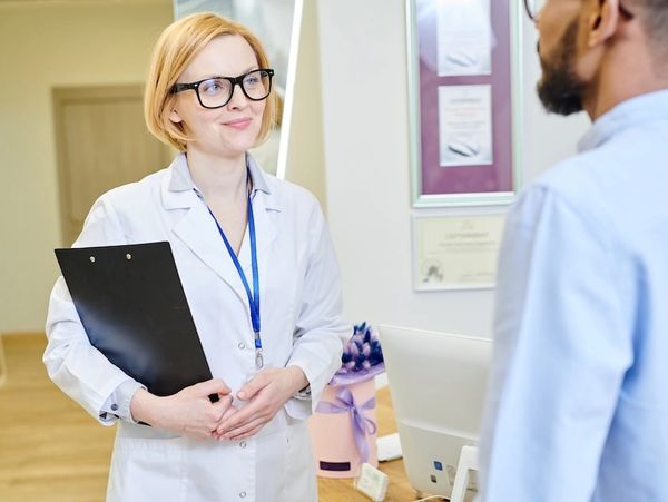 Female doctor with clipboard talking to a male patient in a medical office.