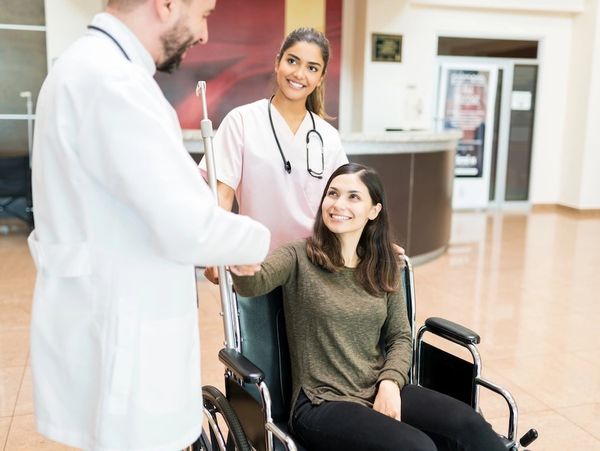 Patient in wheelchair shaking hands with doctor, nurse smiling behind.