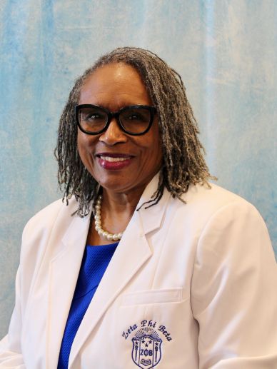 Smiling woman in glasses wearing a white Zeta Phi Beta blazer.