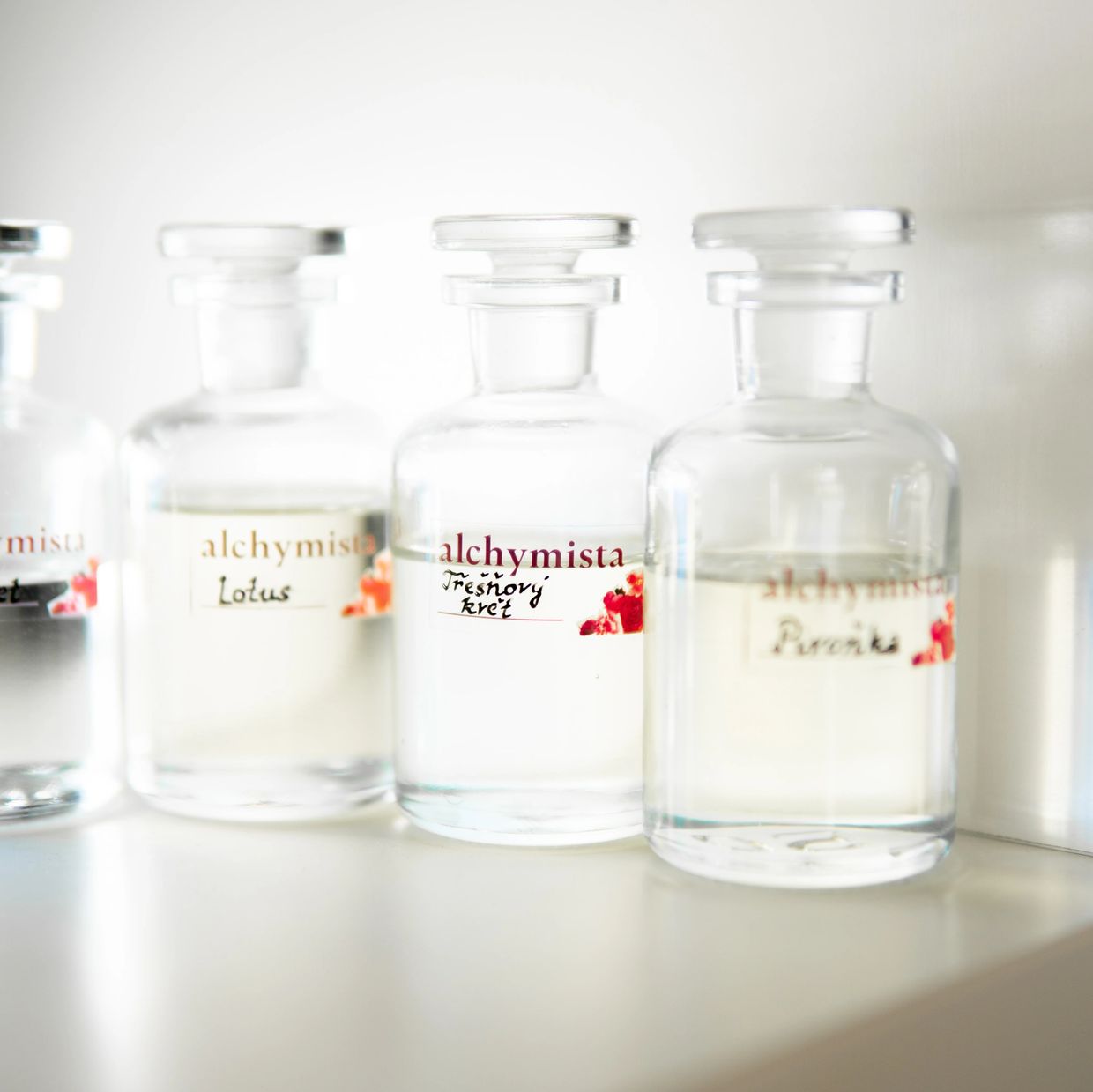 Clear glass bottles with labels of different scents on a white shelf.