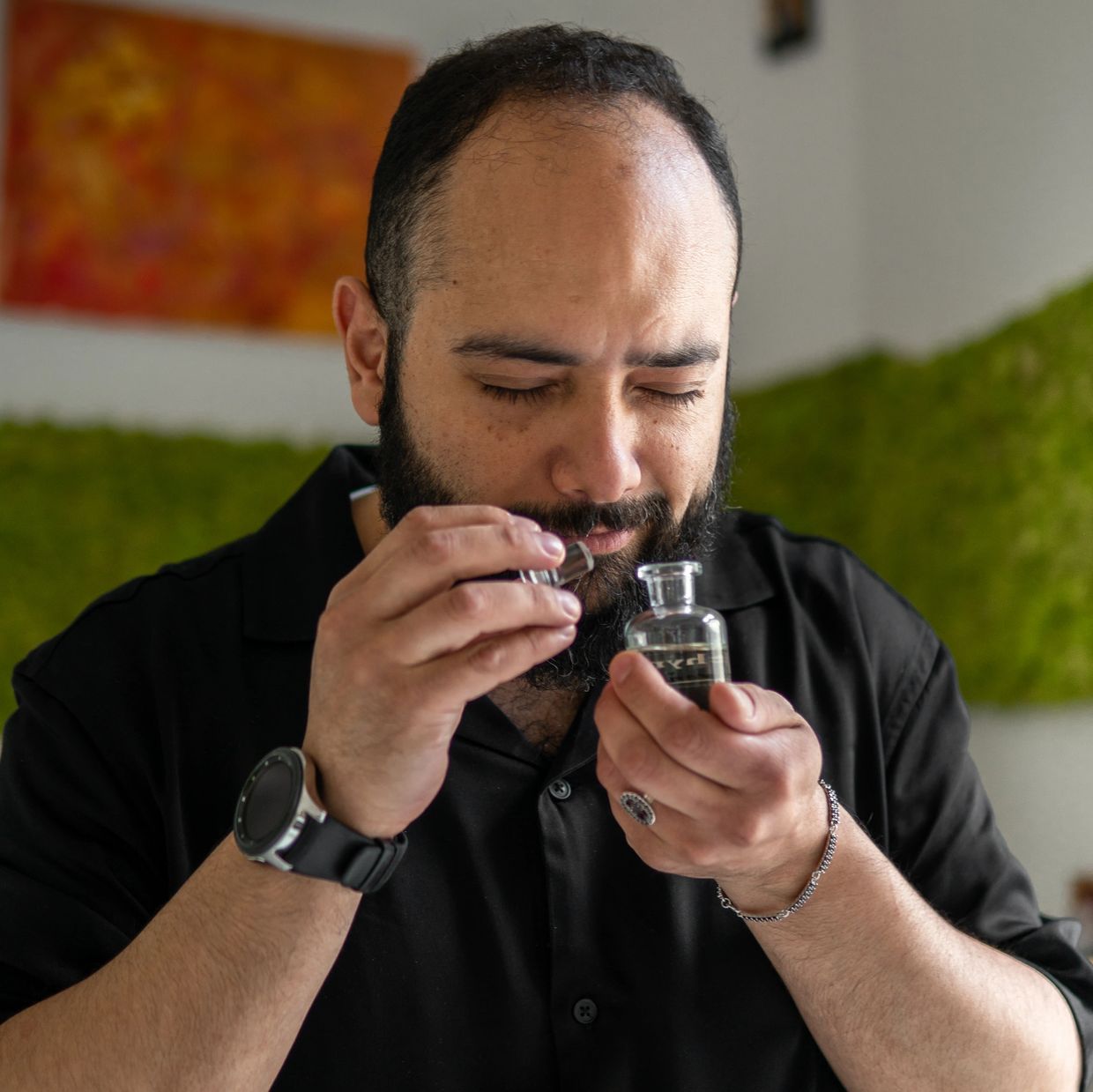 A man smelling a fragrance from a small glass bottle with eyes closed.