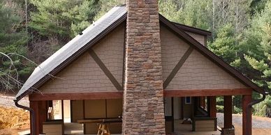 Mountain-style home exterior with stone chimney and covered porch surrounded by trees