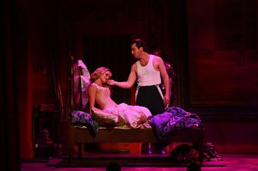 Actors in a romantic theater scene with dim lighting and vintage costumes.