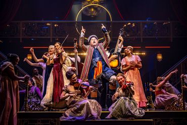 A lively theatrical musical performance with actors in period costumes playing instruments and singing.