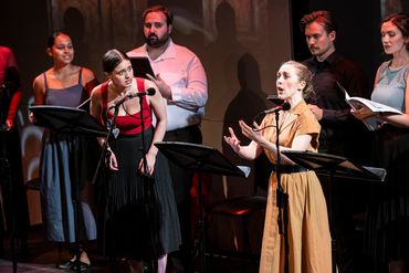 Actors performing a staged reading with microphones and scripts on stands.