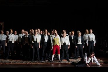 A group of men in historical costumes with one person kneeling in front on stage.