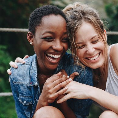 Two women laughing joyfully, sharing a warm moment together outdoors.