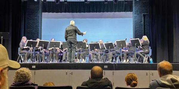 Orchestra performance with conductor leading musicians on stage in front of an audience.