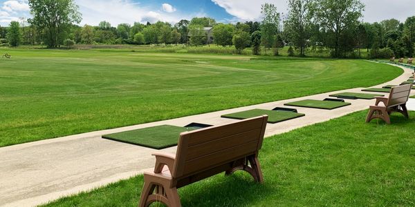 Golf practice mats and benches on a green driving range under a blue sky.