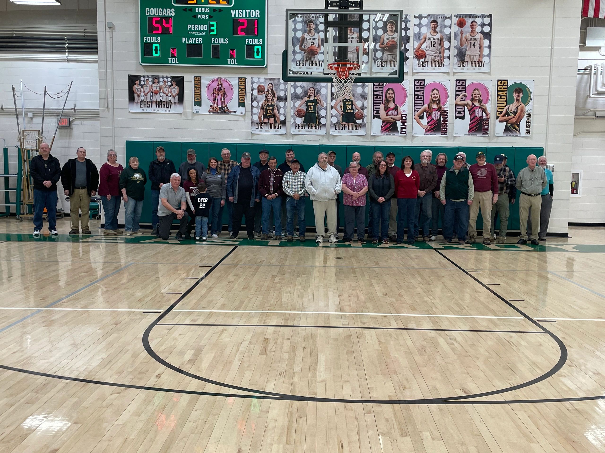 Group photo of people in a gymnasium under a basketball hoop.