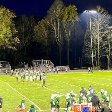 Night football game under bright lights on a grassy field.