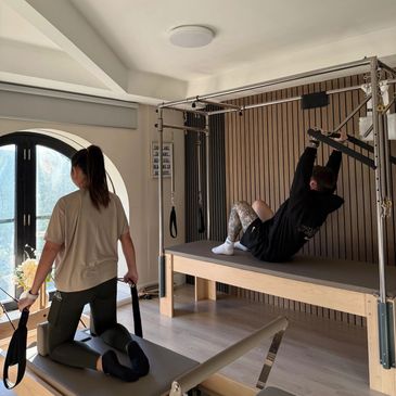 Two people exercising on Pilates equipment in a bright studio.