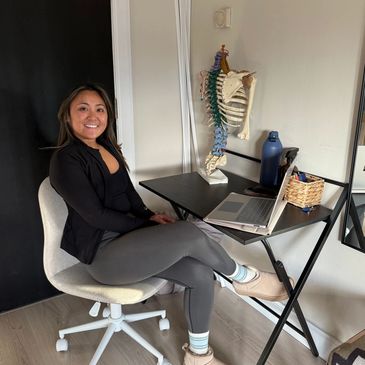 Woman sitting at a small desk with a laptop and anatomical spine model.