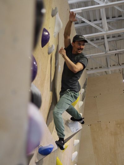 Man climbing an indoor rock climbing wall with focused expression.