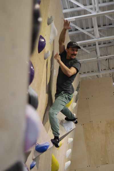 Man climbing an indoor rock climbing wall with focused expression.