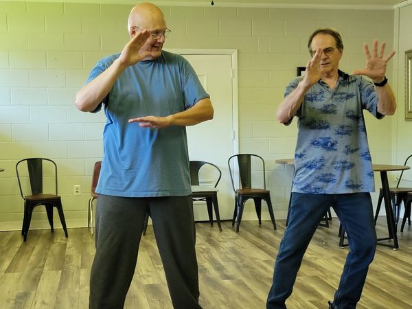 Two men practicing Tai Chi in a spacious room with wooden floors.