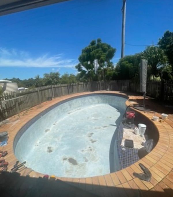 Empty kidney-shaped pool under renovation on a sunny day.