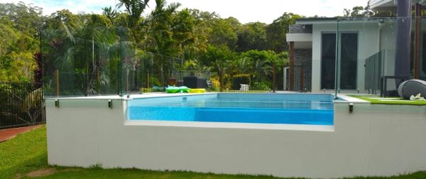 Modern raised pool with clear glass fence in a backyard.