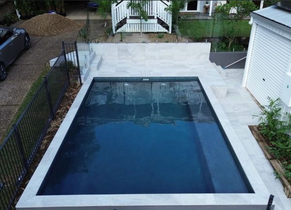 Modern rectangular swimming pool with white tiled surroundings.