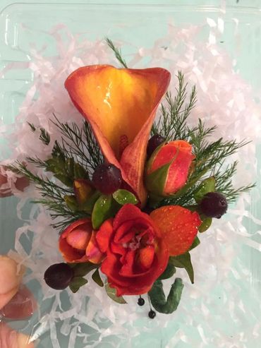 A dark orange boutonniere with greenery