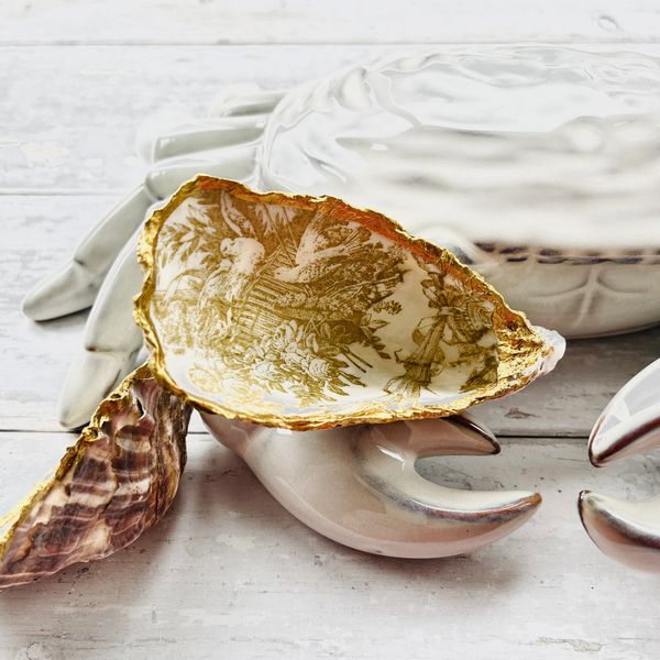 Decorative oyster shell with gold trim resting on a ceramic crab claw.