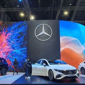 White Mercedes EQS showcased at an auto event with vibrant background screens.