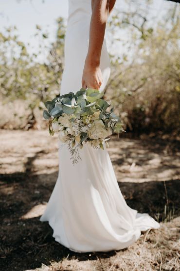 Mariée en robe blanche tenant un bouquet champêtre.