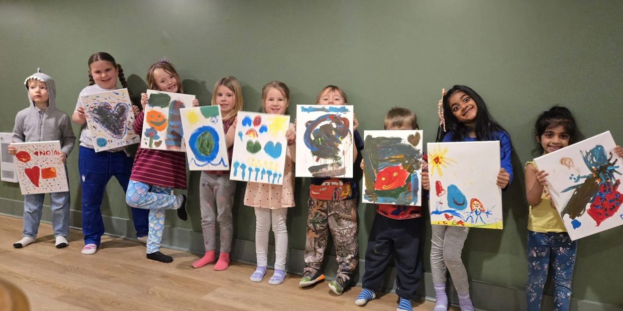 A group of children proudly displaying their colorful paintings indoors.