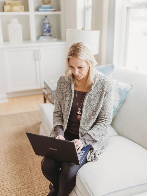 Woman using a laptop while sitting on a couch in a cozy living room.
