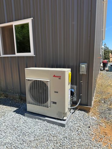 Outdoor Amana HVAC unit installed beside a metal building on gravel.